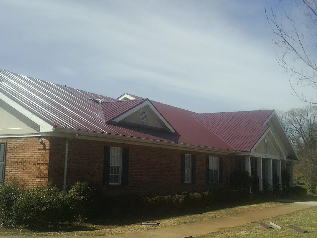 Red metal roof with gabled entries on a long brick building, from a Hail Damage Roof Repair job in Shelocta