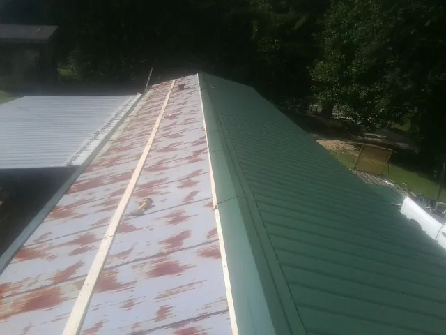 Old rusted panels beside newly installed green metal roofing — Wind Damage Roof Repair by Roofing Brothers in Shelocta