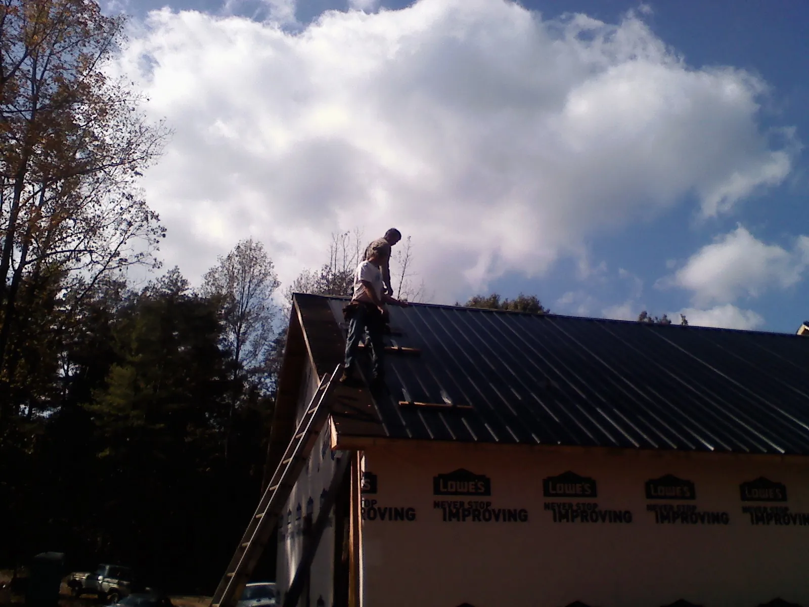 Roofer fastening dark metal panels high against a cloudy sky, from a Roof Inspection job in Shelocta