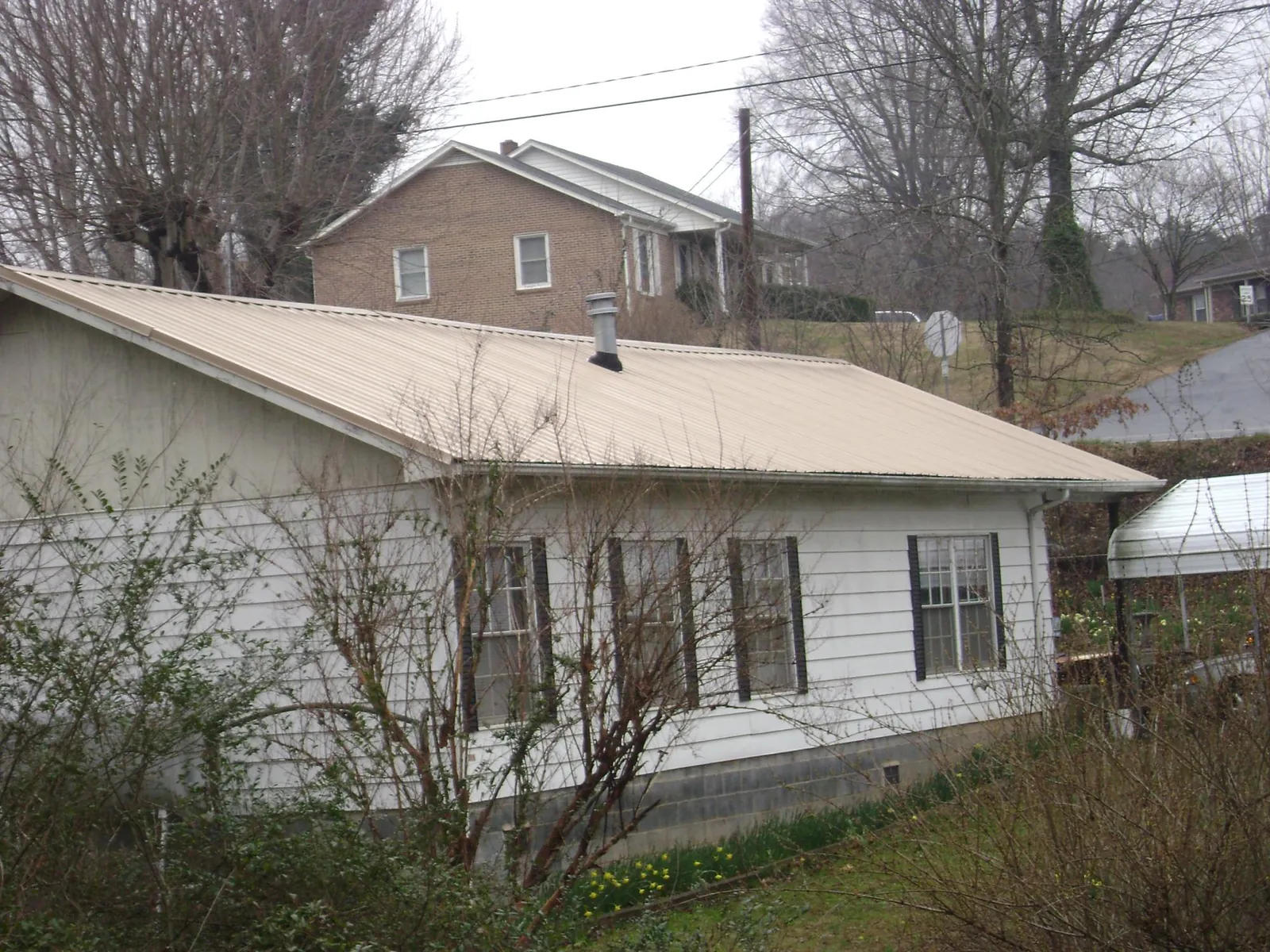 Tan metal roof on a white sided house set into a hillside — Commercial Roofing by Roofing Brothers in Shelocta