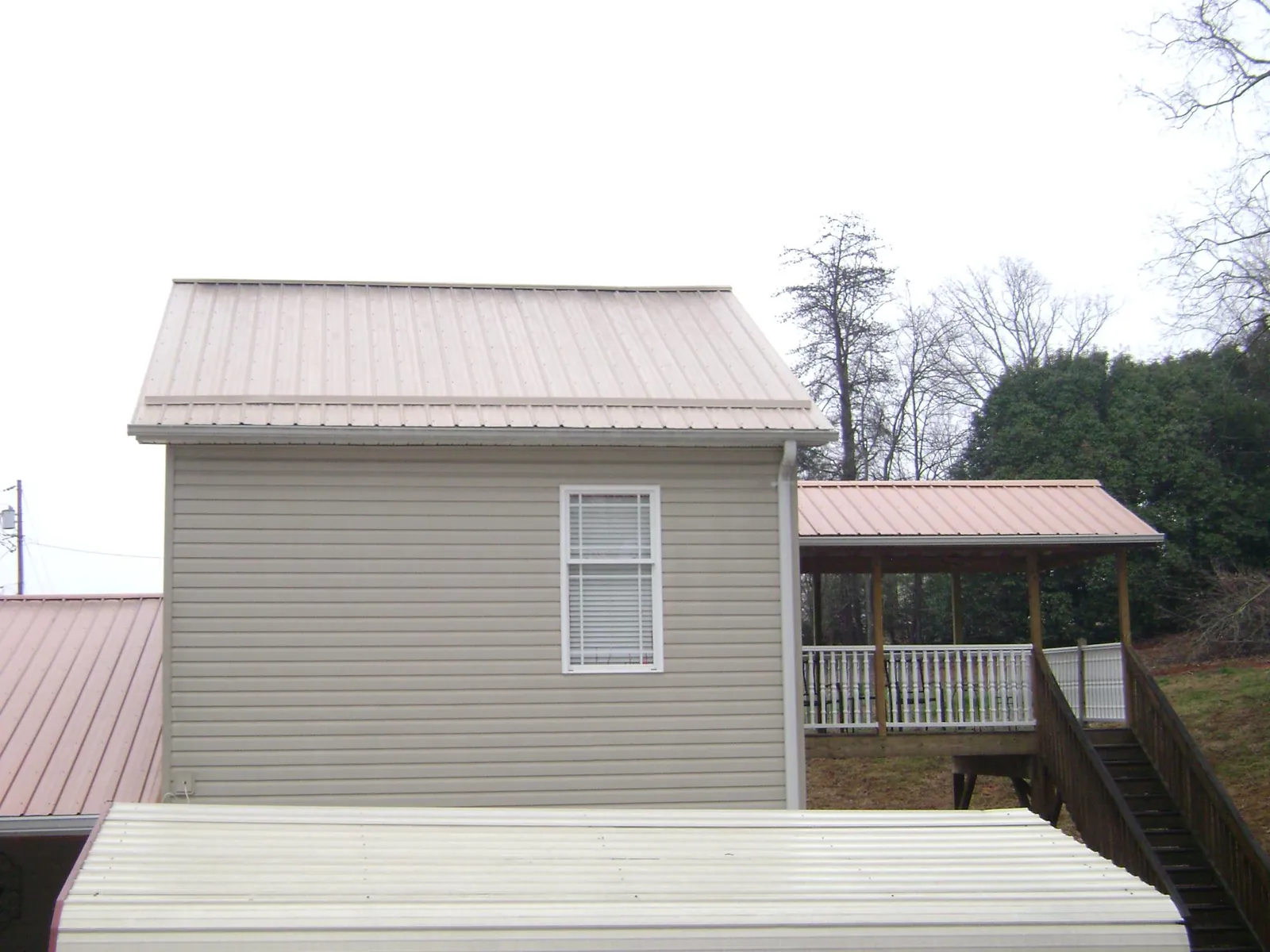 Tan metal roofs on a two story addition and attached porch, from a Roof Replacement job in Shelocta